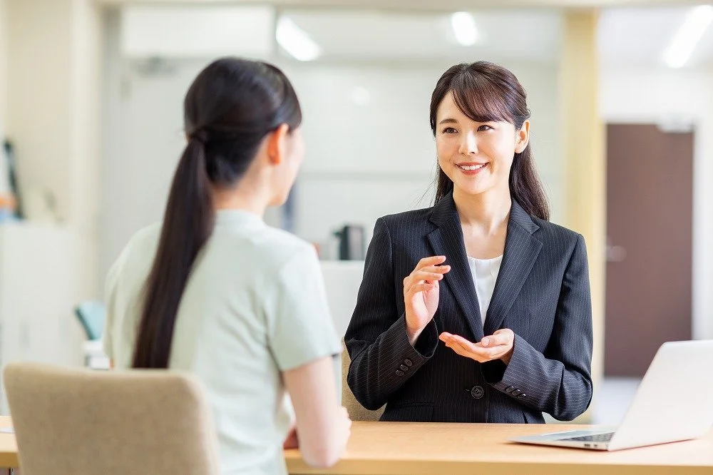 スーツ姿の女性カウンセラーが、笑顔で相談者に説明している様子